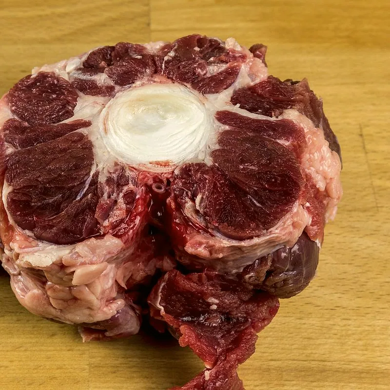 A raw piece of oxtail, a cross-section of dark red meat around a central bone