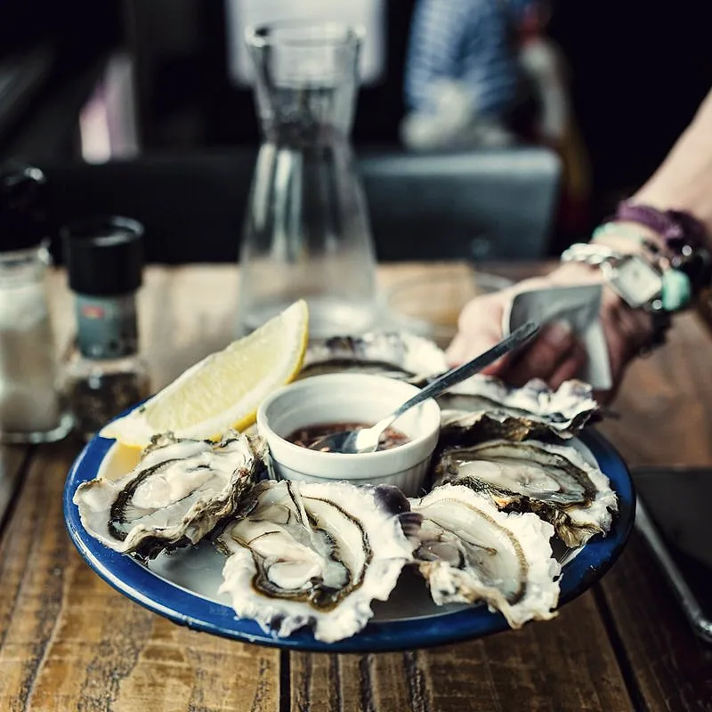 A plate of freshly shucked raw oysters on the half shell with a lemon wedge and mignonette sauce