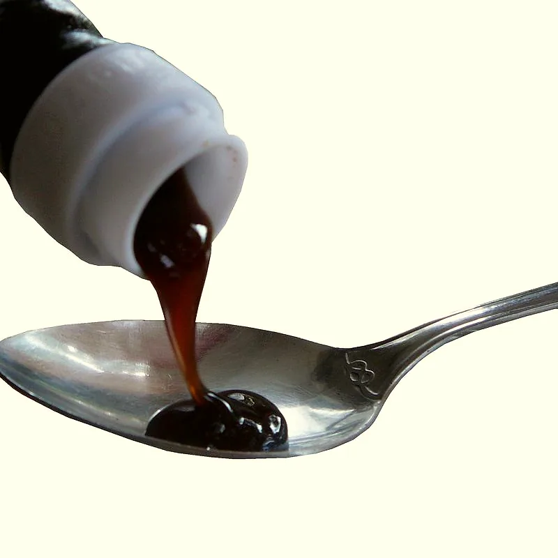 Thick, dark brown oyster sauce being poured from a bottle onto a metal spoon