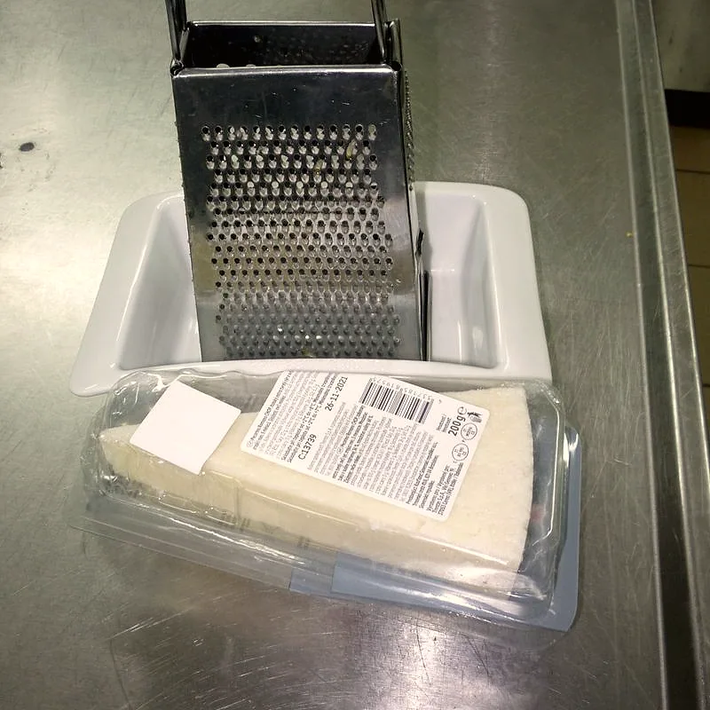 A wedge of hard pale Pecorino Romano beside a box grater