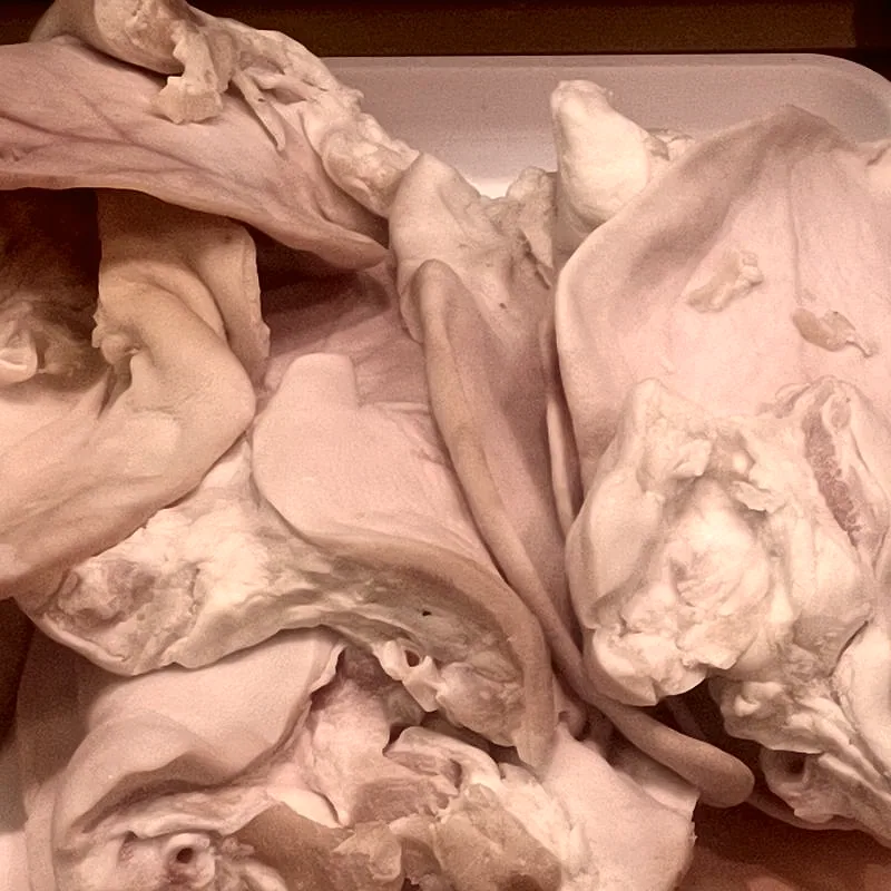 A pile of raw, pale pink pig ears in a tray