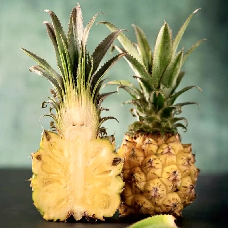 A whole pineapple beside a halved pineapple showing its yellow flesh