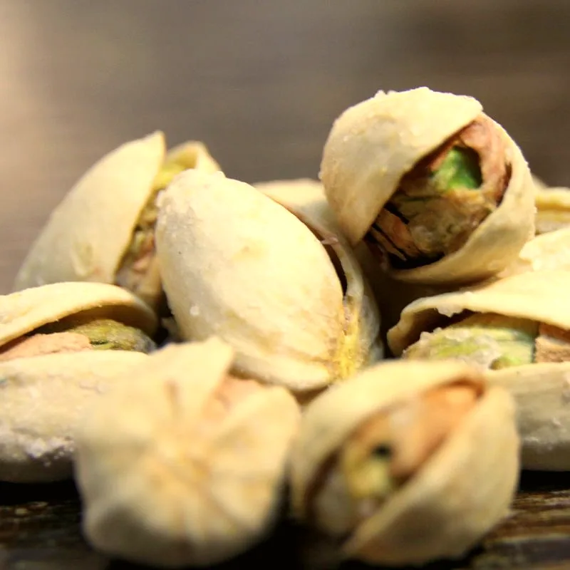 A pile of pistachios with their shells split open, showing the green kernels inside