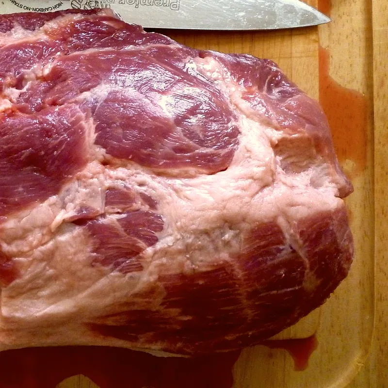 A raw whole pork shoulder joint on a cutting board