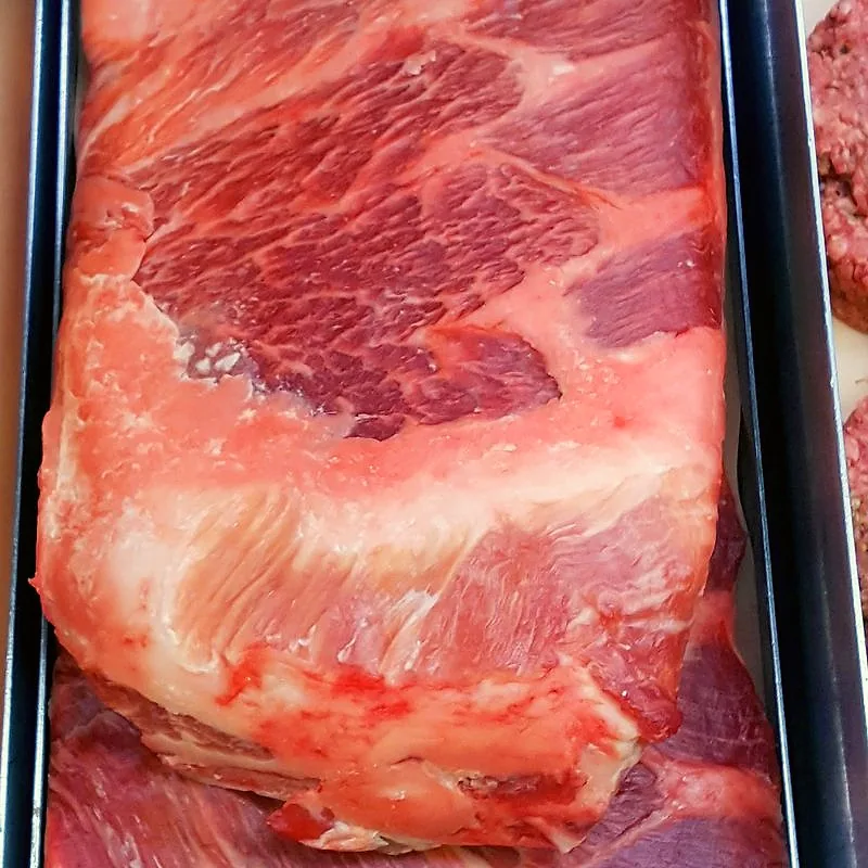A raw slab of pork spare ribs in a butcher's tray, showing the flat rib section with fat cap