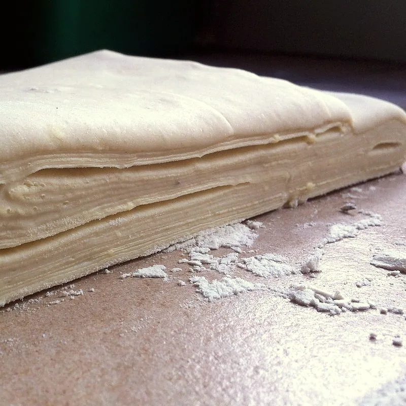 A close-up cross-section of raw puff pastry, showing its many thin laminated layers on a floured surface