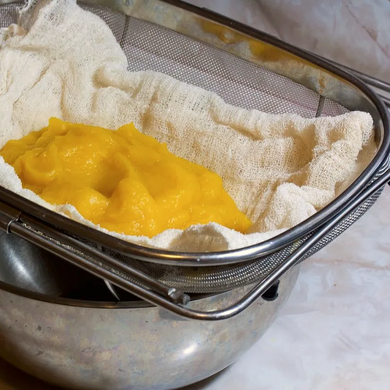 Bright orange pumpkin puree draining in cheesecloth set inside a metal strainer