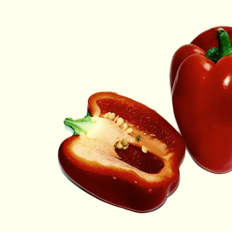 A whole red bell pepper beside one cut open, showing the pale ribs and seeds