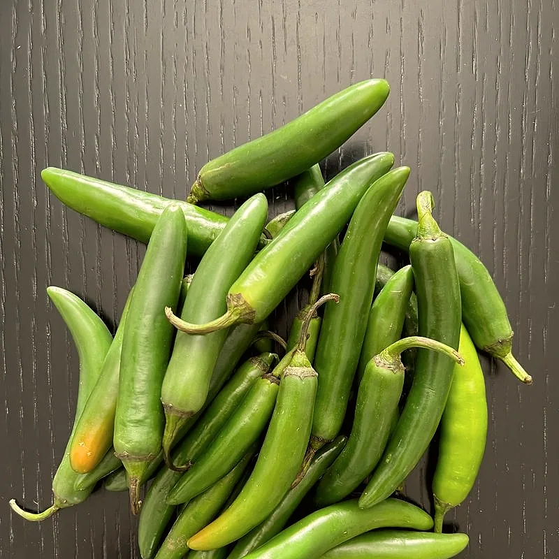A heap of small green serrano chillies, smooth and blunt-tipped