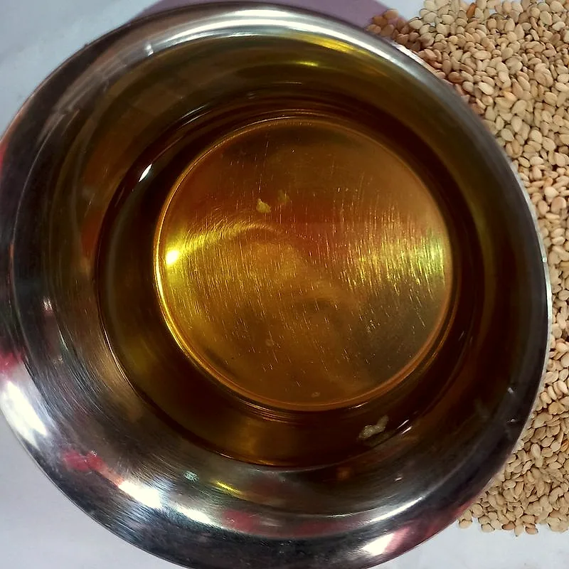 Sesame oil in a steel bowl beside a heap of sesame seeds