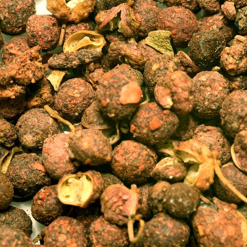 A close-up pile of dried reddish-brown Sichuan peppercorns, some split open showing the husks