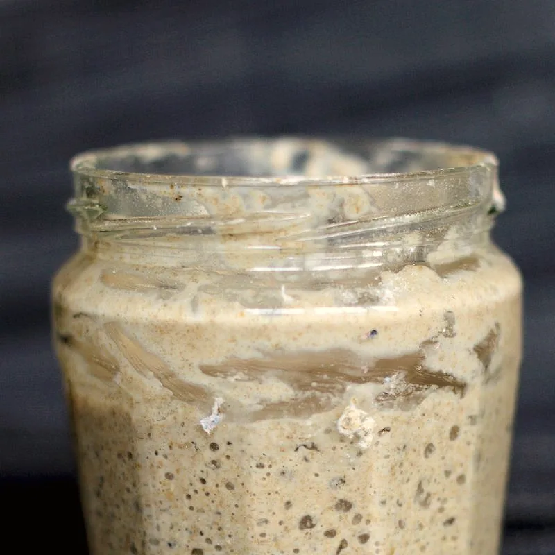 A glass jar of bubbly, active sourdough starter with visible air pockets