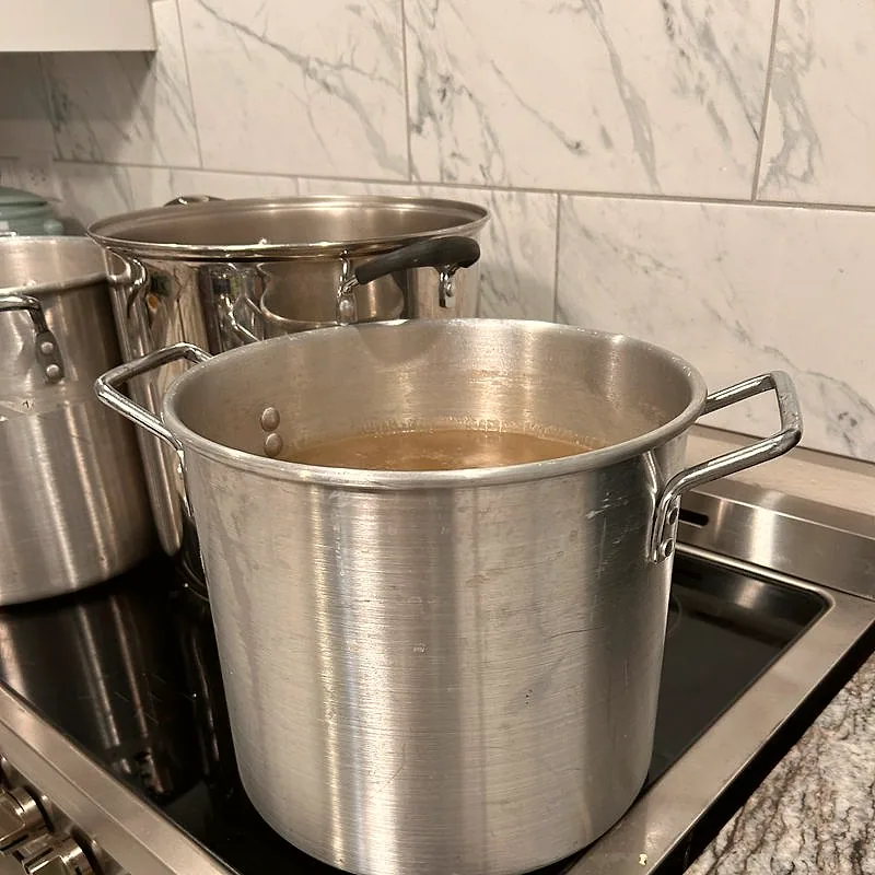 A large steel pot of amber-coloured stock simmering on a stove