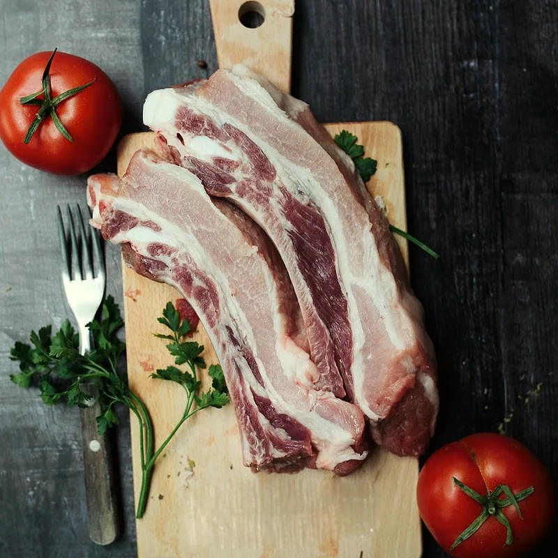 Raw streaky bacon rashers with visible fat and lean striping, on a wooden board with parsley and tomatoes
