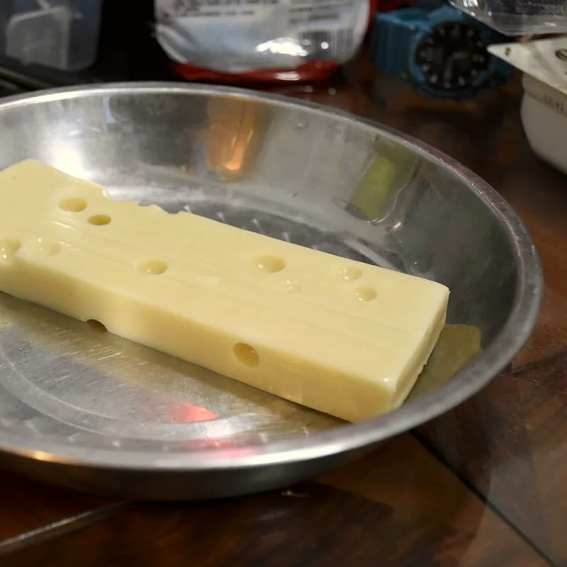 A block of pale yellow Swiss (Emmental) cheese with characteristic round holes, in a metal dish