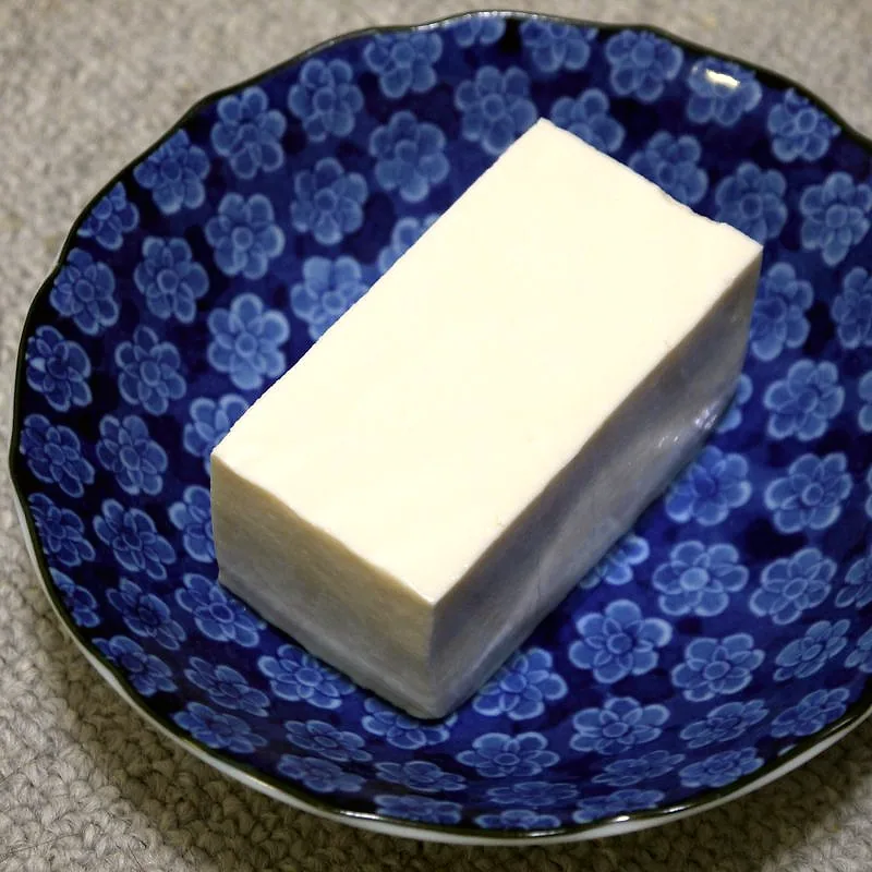 A pale white block of silken tofu on a blue-patterned plate
