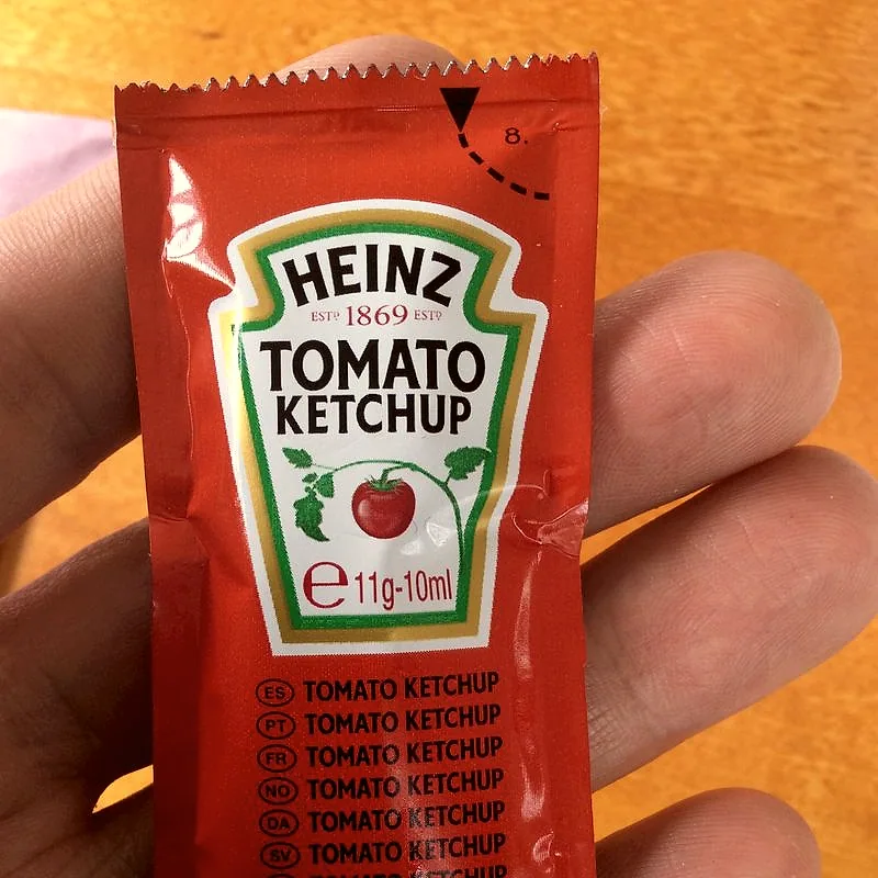 A glossy dollop of dark red tomato ketchup on a plain surface
