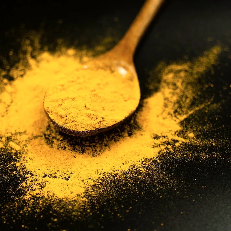 A wooden spoon heaped with bright yellow-orange turmeric powder