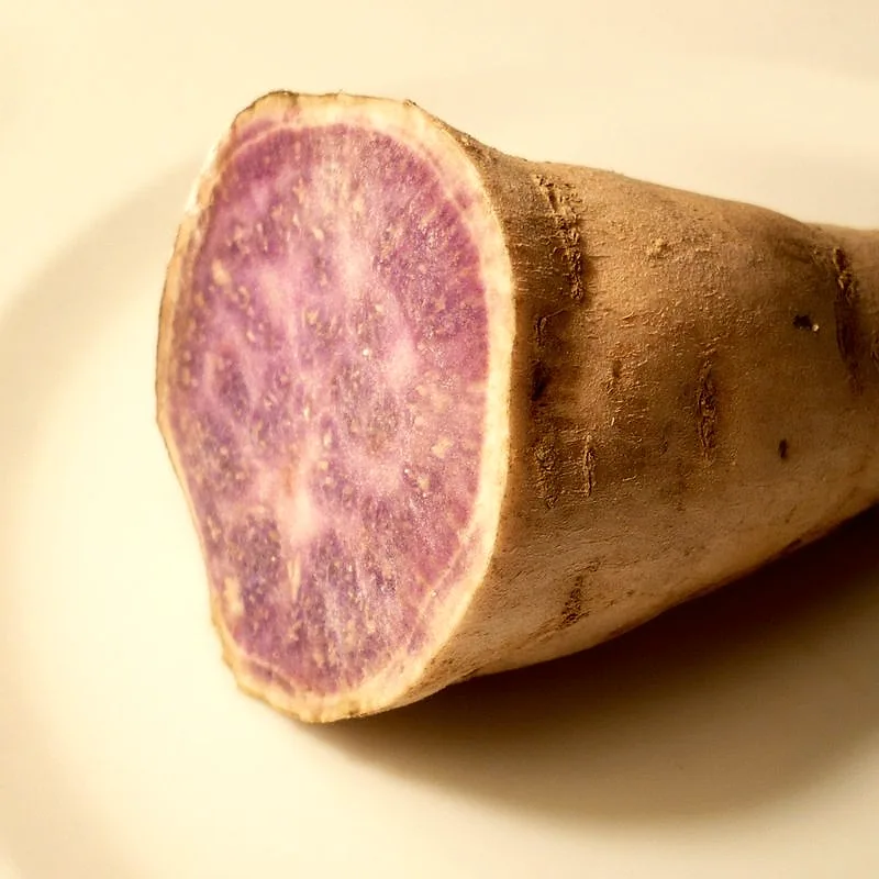 A whole raw ube tuber with brown skin, cut to reveal its vivid purple flesh