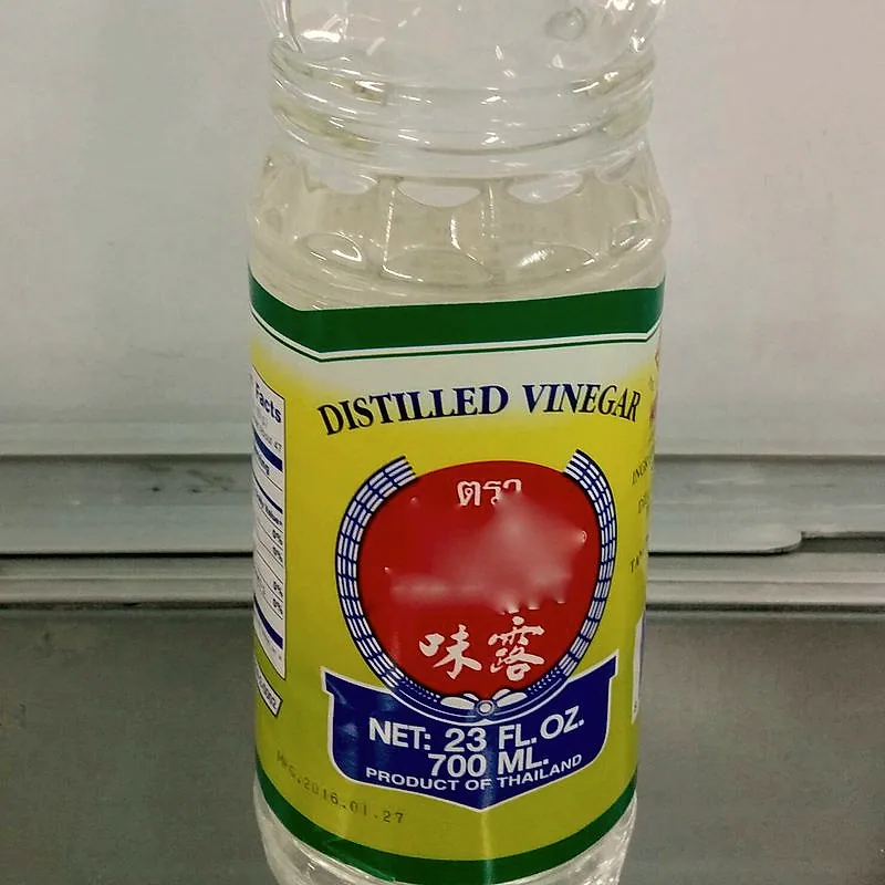 A clear plastic bottle of distilled white vinegar, showing the clear liquid above the label