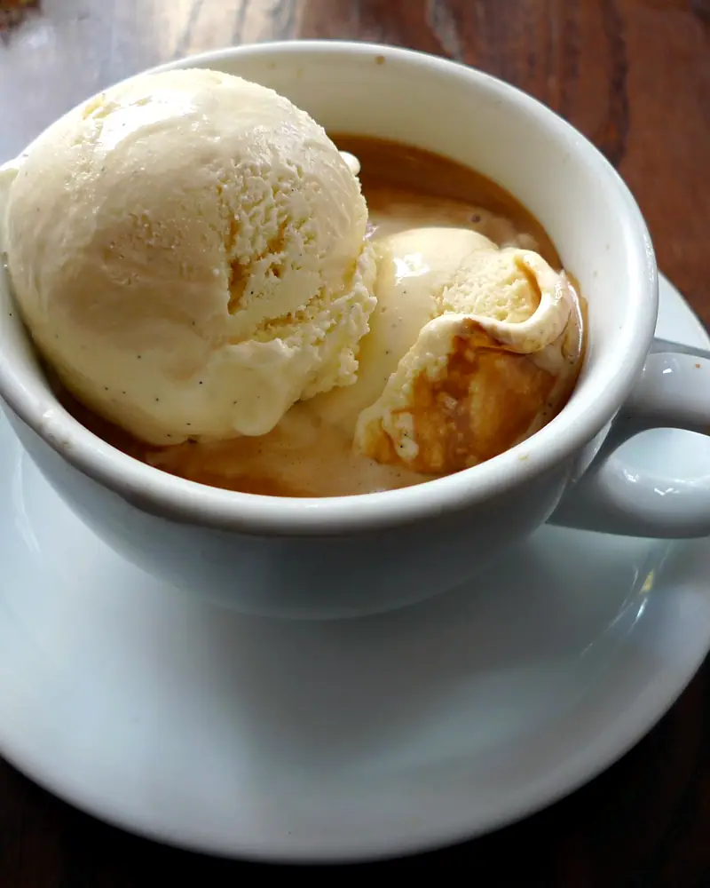 A scoop of vanilla ice cream melting into espresso in a white cup, affogato al caffè
