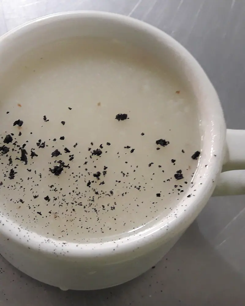 Pale, thick atole in a white mug, dusted with dark ground spice
