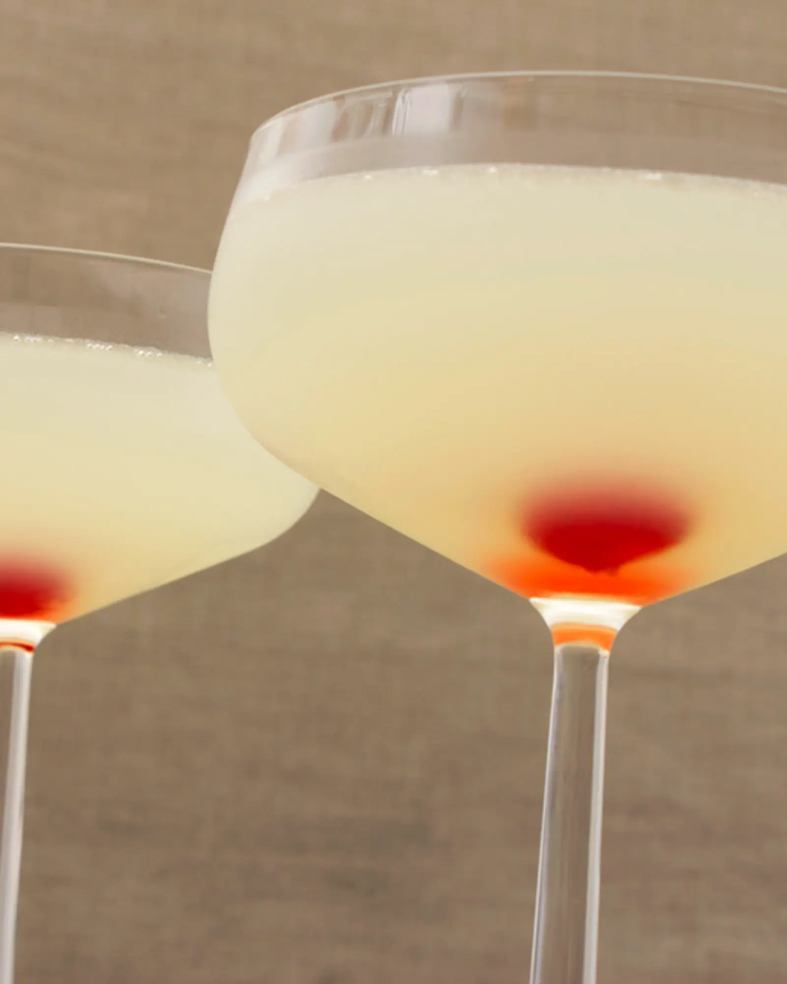 Two pale straw-coloured Aviations in coupe glasses, each with a maraschino cherry resting at the base