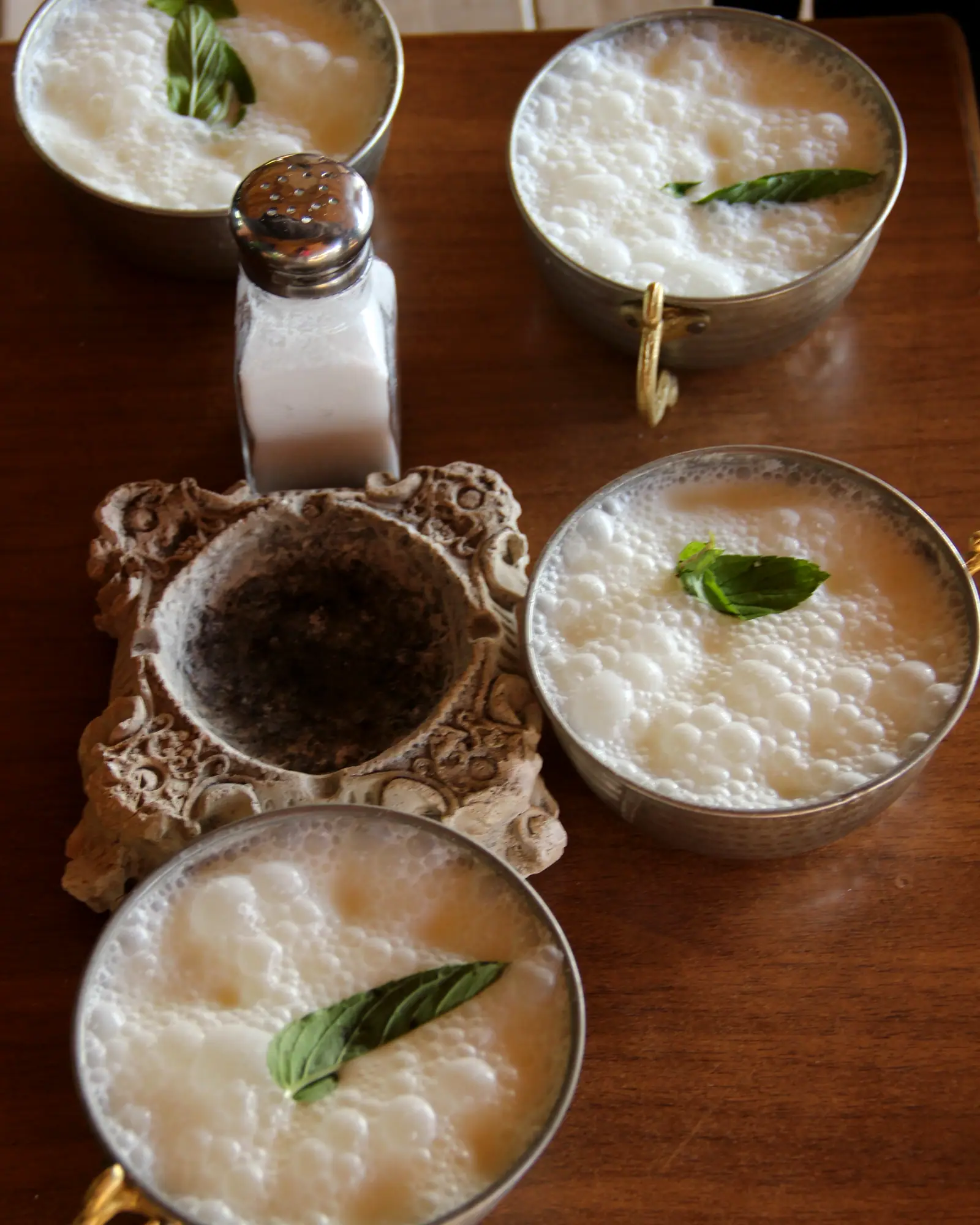 Foamy white ayran in metal cups garnished with fresh mint leaves, seen from above