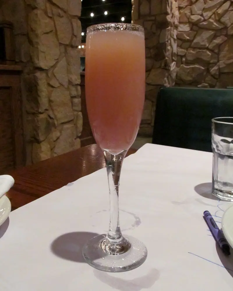 A pink-orange Bellini in a champagne flute on a white tablecloth