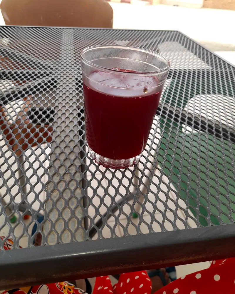 A clear cup of deep red hibiscus drink, zobo, served on an outdoor table