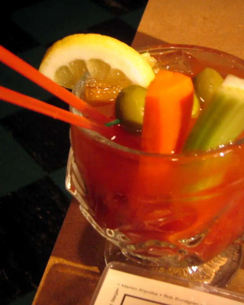 A Bloody Mary garnished with a lemon wheel, green olives, a carrot stick and celery, with red straws