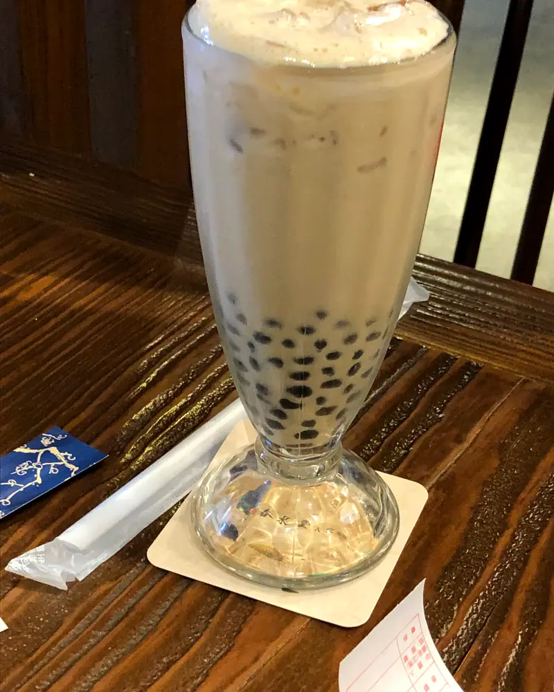 Milky bubble tea in a tall glass, black tapioca pearls settled at the bottom
