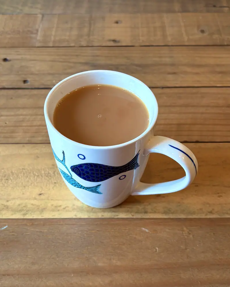 A white mug filled with strong, milky tea on a wooden table