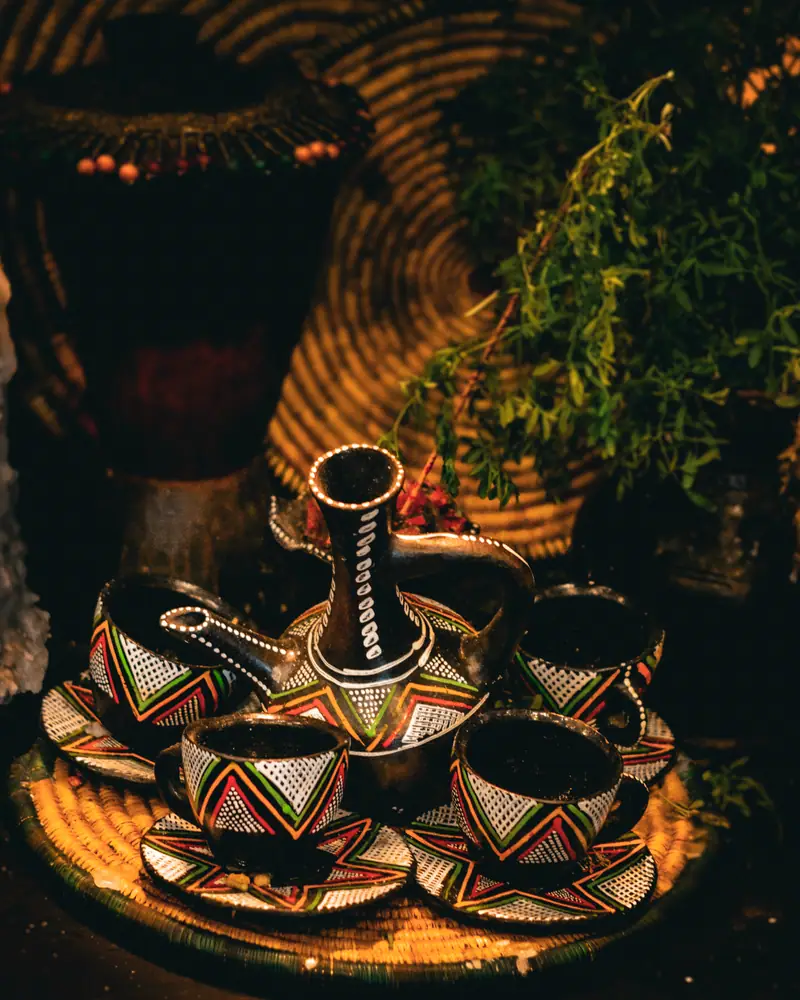 A clay jebena coffee pot on a woven tray, surrounded by small painted cups for an Ethiopian coffee ceremony