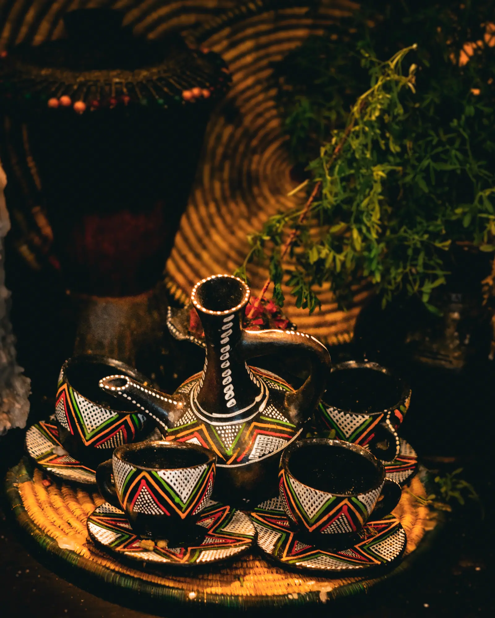 A clay jebena coffee pot on a woven tray, surrounded by small painted cups for an Ethiopian coffee ceremony