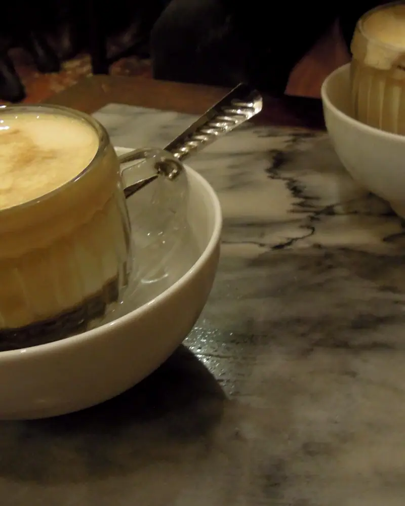 A small glass of Vietnamese egg coffee with a whipped, pale foam top, set in a bowl of hot water