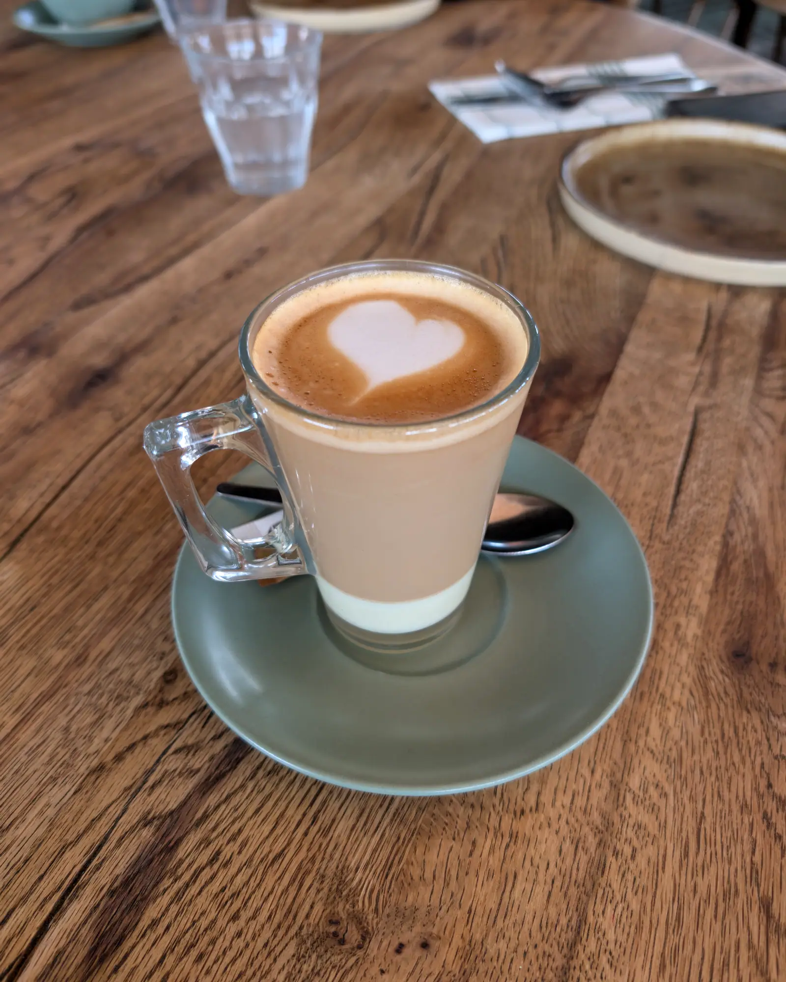 Café con leche with a heart of latte art, in a glass mug on a saucer