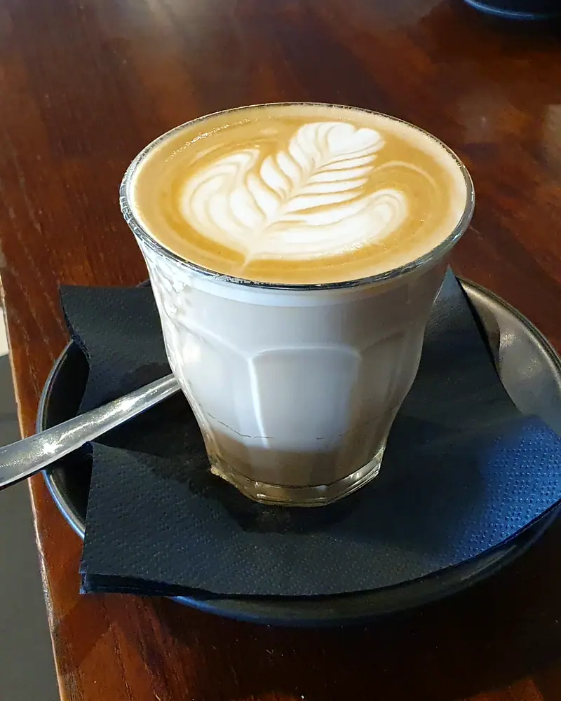 A caffè latte in a glass cup with a leaf pattern in the milk foam