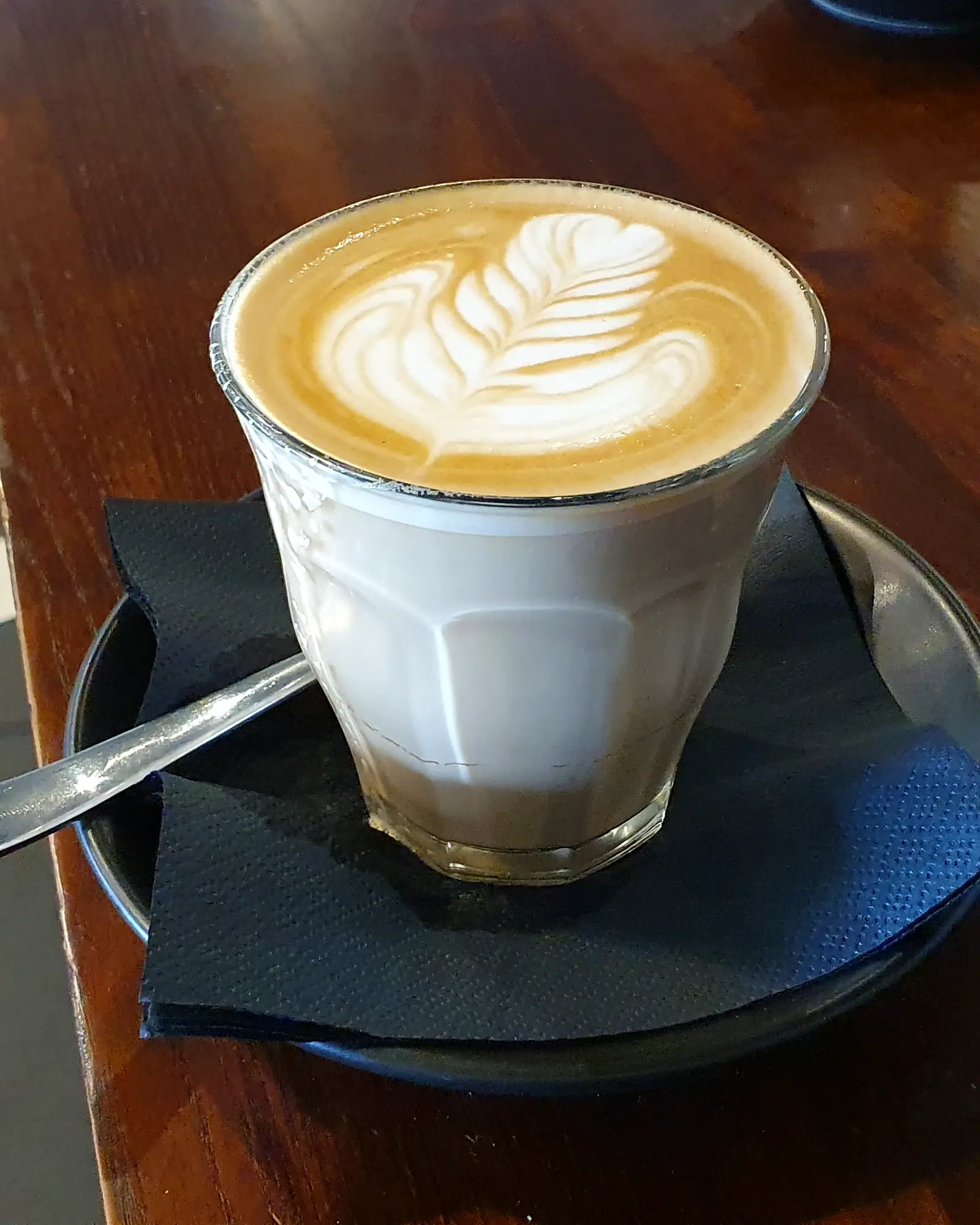 A caffè latte in a glass cup with a leaf pattern in the milk foam