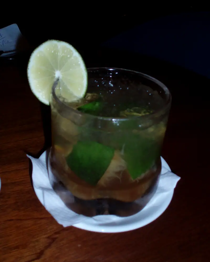 A caipirinha in a rocks glass, muddled lime wedges and ice, garnished with a lime wheel