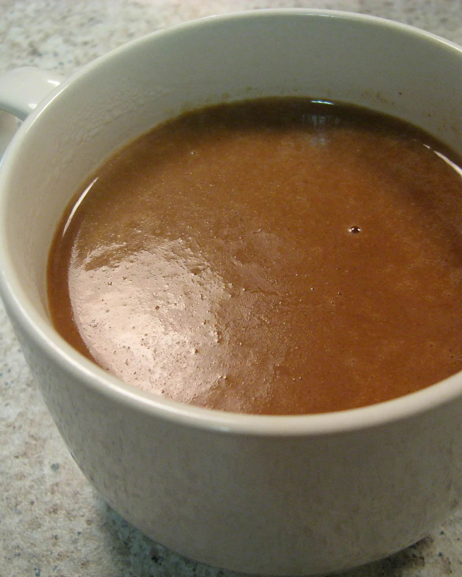 Thick chocolate-brown champurrado filling a white mug