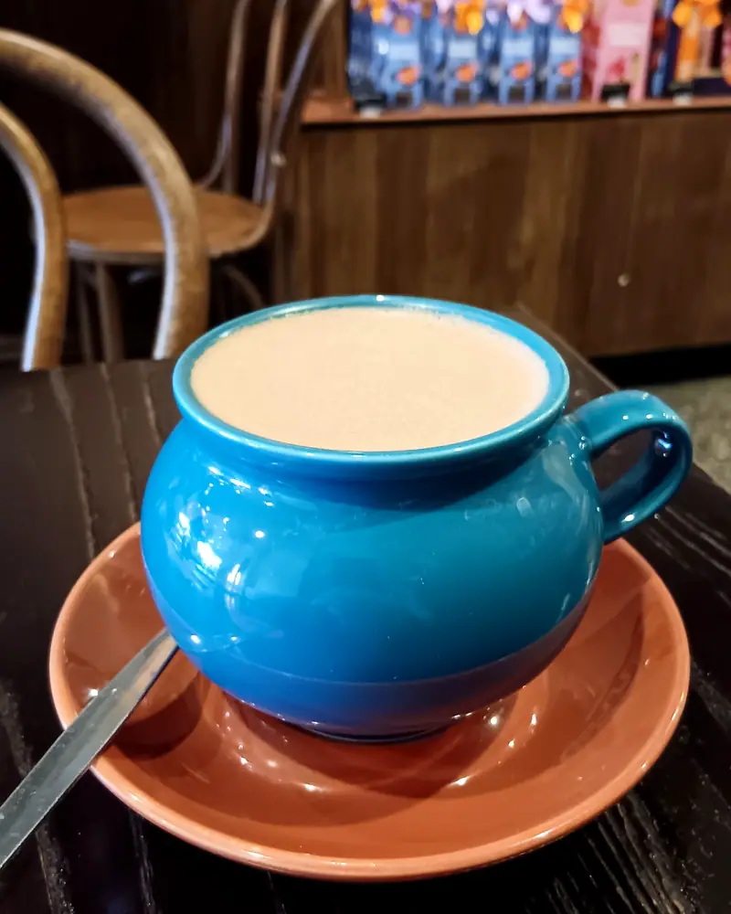 Frothy hot chocolate filling a blue ceramic mug on a terracotta saucer