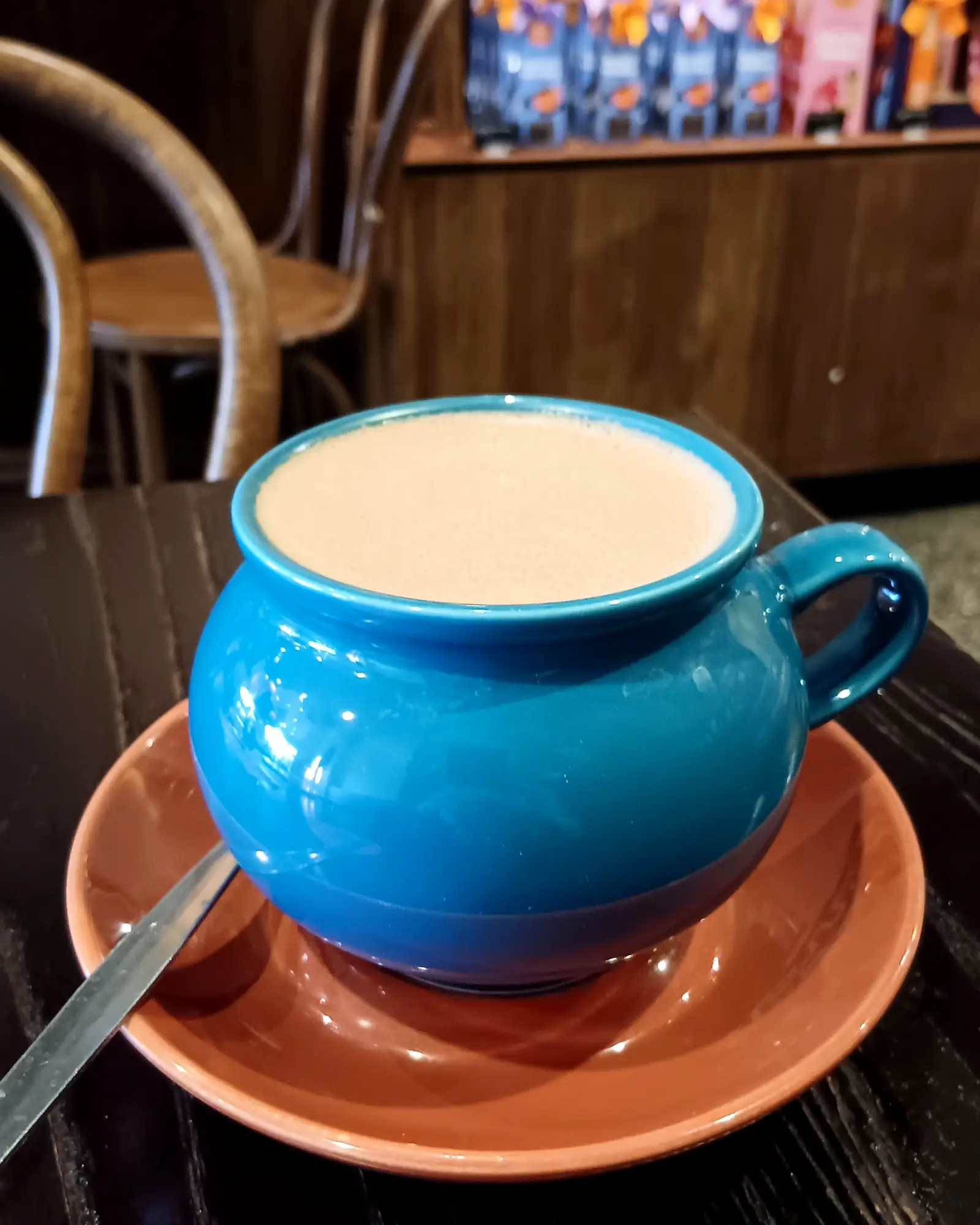Frothy hot chocolate filling a blue ceramic mug on a terracotta saucer