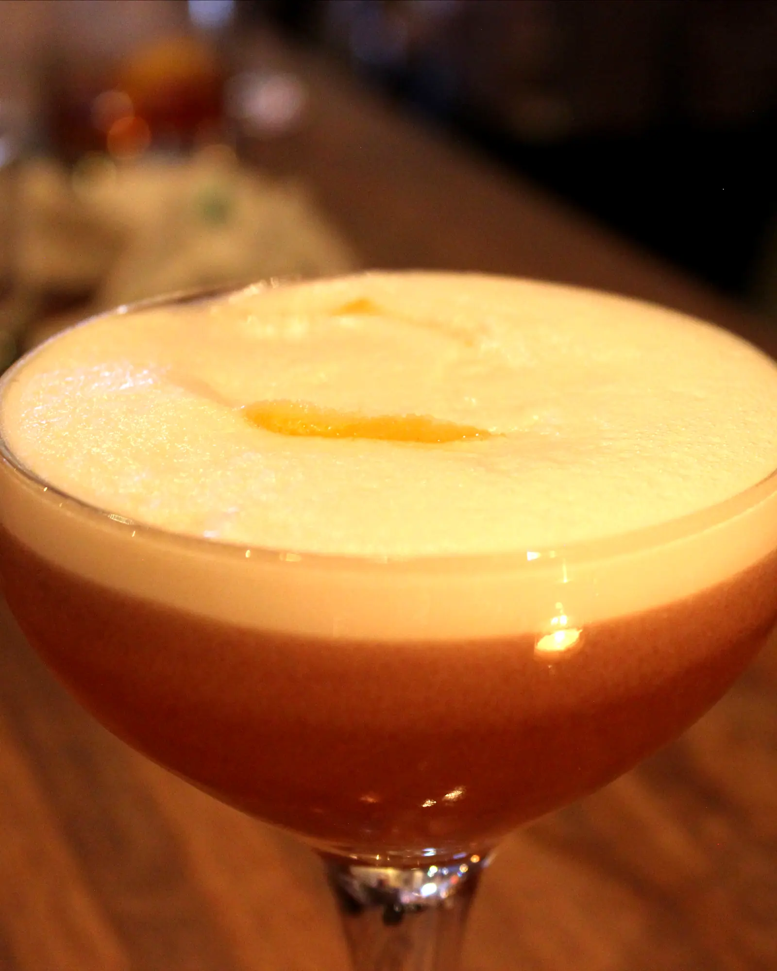 A Clover Club cocktail in a coupe, layered pink beneath a dense white foam, garnished with a raspberry on the surface