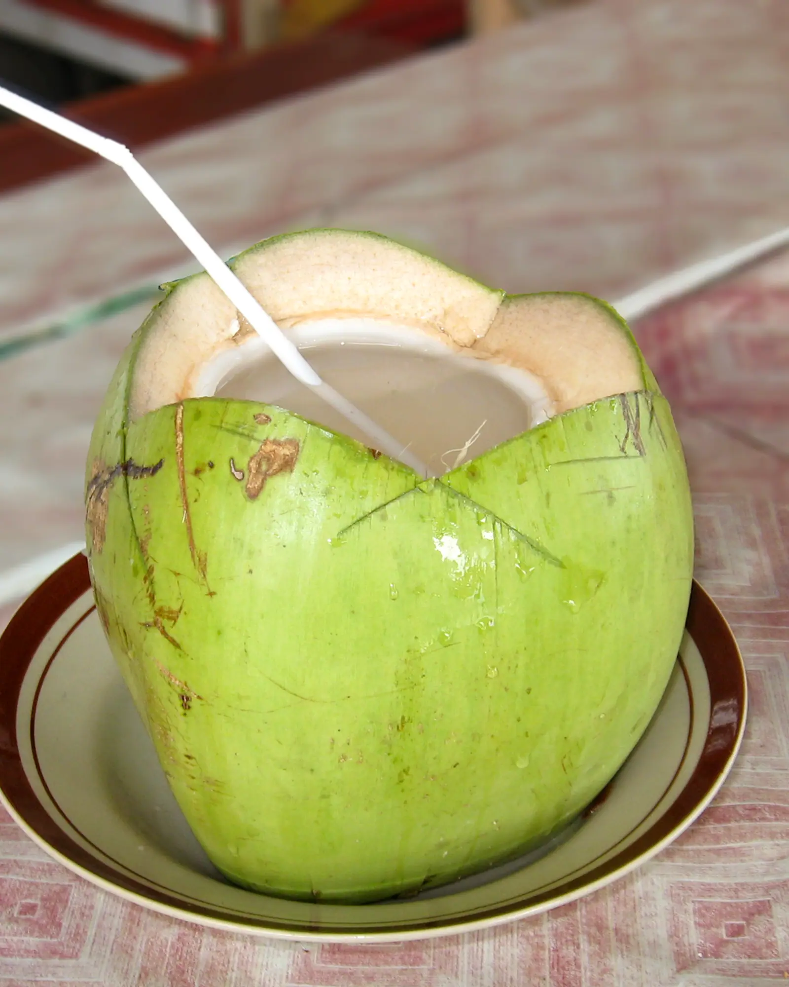 A young green coconut opened at the top with a straw, ready to drink