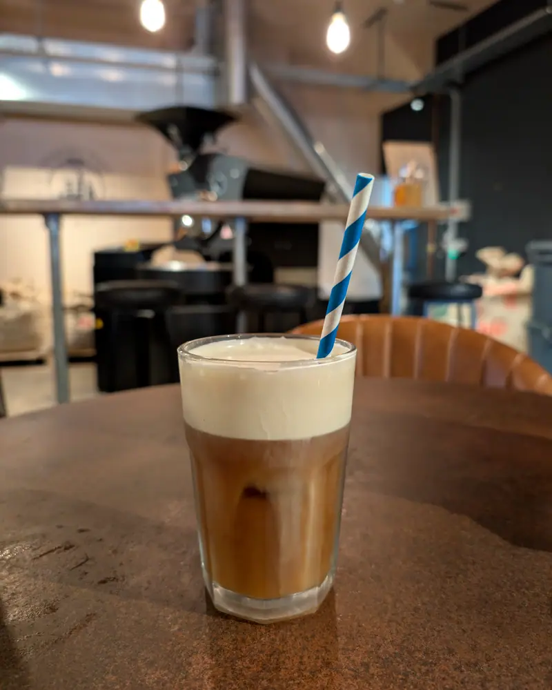 Cold brew coffee in a glass, dark coffee under a pale cream float, with a striped straw