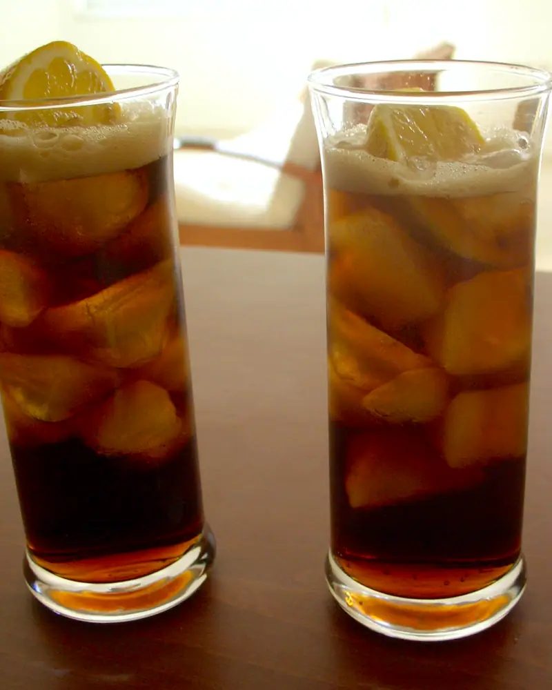 Two tall glasses of Cuba Libre, dark rum and cola over ice, garnished with a citrus wedge