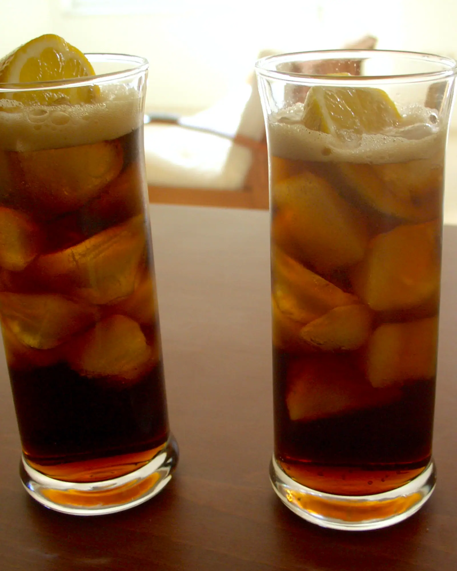 Two tall glasses of Cuba Libre, dark rum and cola over ice, garnished with a citrus wedge