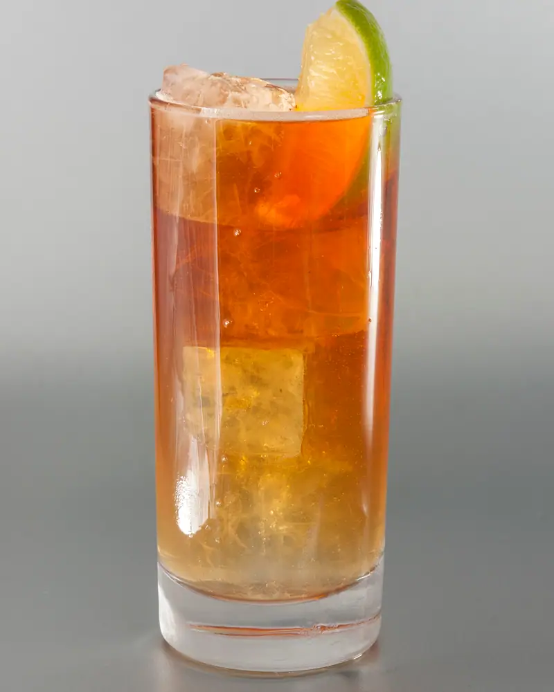 A Dark and Stormy in a tall glass over ice, the dark rum still visible unmixed above the paler ginger beer, garnished with a lime wedge