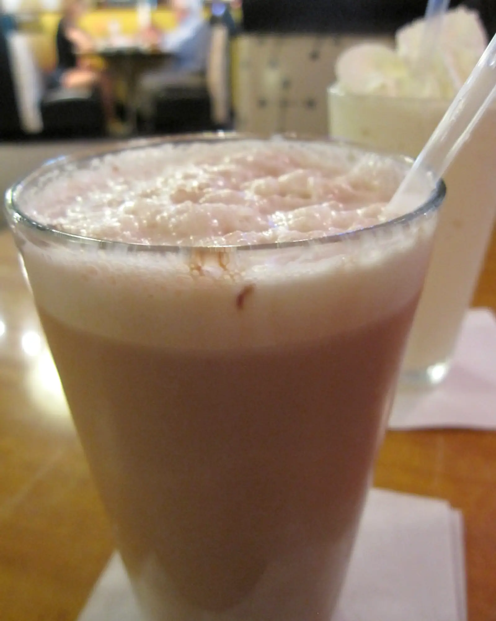 A chocolate egg cream in a plain glass, with a thick pale foam head and a straw